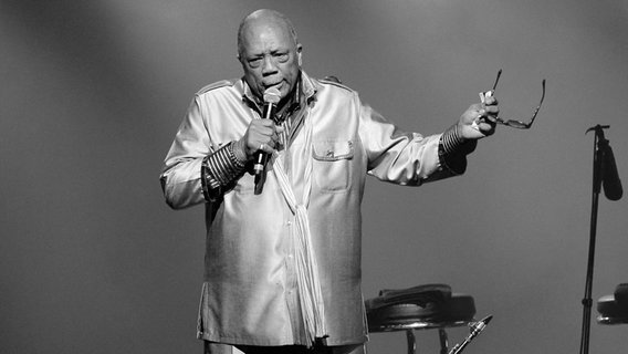 Der Musiker Quincy Jones steht auf einer Bühne und hält ein Mikro und seine Brille in den Händen © picture alliance / abaca | Python Jean-Guy/ABACA Foto: Python Jean-Guy