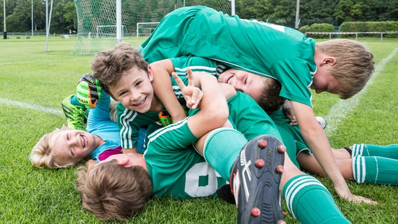 Eimn Gruppe von Kindern in grünen Trikots liegen auf dem Rasen. © Imago / Westend61 Foto: Imago / Westend61