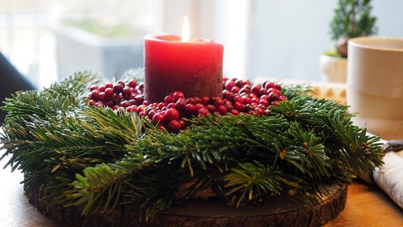 Eine schlichte roten Stumpenkerze in einem Adventskranz aus Tannengrün mit roten Beeren dekoriert. © NDR Foto: Anja Deuble