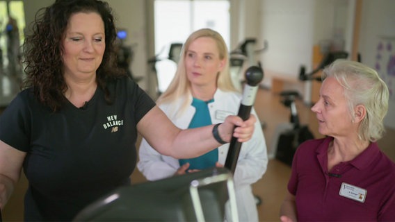 Patientin Jennifer S. in Bewegung auf einem Crosstrainer. Bewegungs-Docs Melanie Hümmelgen und Sportlehrerin Frau Krampe leiten sie an. © NDR Foto: Screenshot