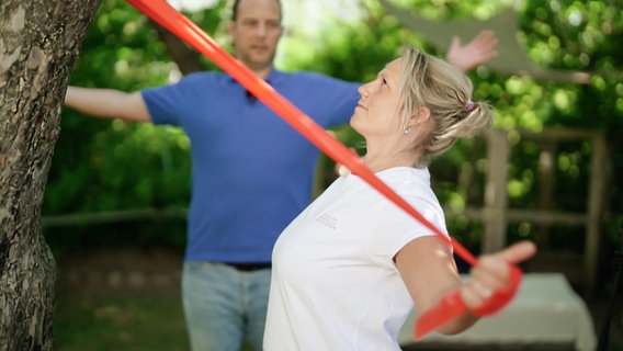 Patientin Cathrine P. führt Dehnübungen mit einem Theraband durch. © NDR Foto: Screenshot