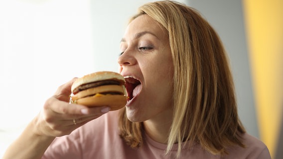 Eine Frau beißt in einen Burger. © Colourbox 