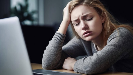 Burnout: Eine junge Frau sitzt verzweifelt vor einem Laptop und stützt den Kopf in die Hand. © IMAGO/ imageBROKER Foto: Paul Hartl