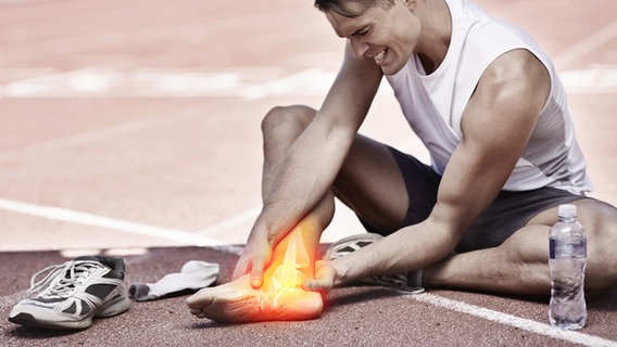 Mann in Sportkleidung sitzt mit schmerzverzerrtem Gesicht auf Laufbahn und hält sich den Fuß (Bild: colourbox.de/Peoplesimages.com) © colourbox.de/Peoplesimages.com 