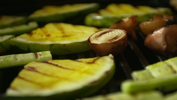 Melonenstücke, Gurken und Zwiebeln liegen auf einem Grill. © NDR 