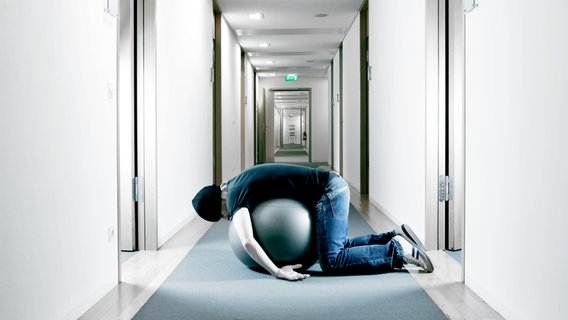 Ein Mann liegt in einem Büroflur auf einem Gymnastikball. © Photocase Foto: kallejipp