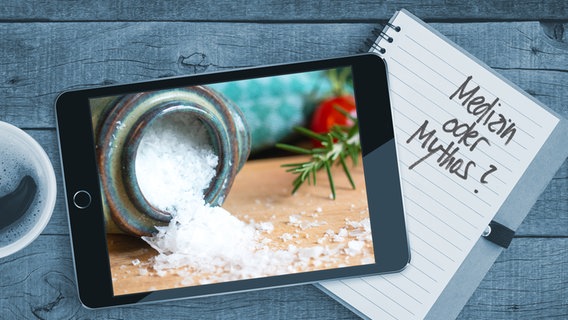 Auf einem Tisch liegt ein Tablet mit einem Bild von einem Salzfässchen aus Ton mit Salzkristallen. Auf einem Notizblock sind die  Worte "Medizin oder Mythos" zu lesen (Montage) © Colourbox Foto: Blackzheep/Anja Deuble