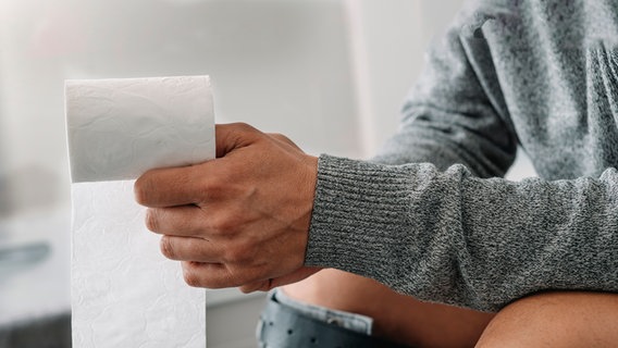 Mann sitzt auf Toilette, in seiner rechten Hand liegt eine Rolle Toilettenpapier (Bild: colourbox.de/Juan Moyano) © colourbox.de Foto: Juan Moyano