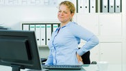 Eine Frau sitzt mit Rückenschmerzen am Schreibtisch. © Picture-Factory/fotolia Foto: Picture-Factory