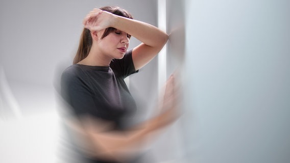 Eine junge Frau stützt sich an einer Wand ab. Ihre Augen sind geschlossen. Der Hintergrund ist teilweise unscharf. © IMAGO / Panthermedia 