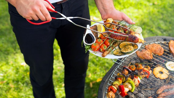 A man puts a sausage and grilled vegetables on a plate.  © fotolia Photo: Photographee.eu