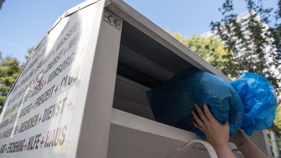 Eine Frau wirft gebrauchte Kleidung in einem Plastiksack in einen Kleider-Container des DRK (gestellte Aufnahme). © picture alliance / dpa-Themendienst Foto: Andrea Warnecke