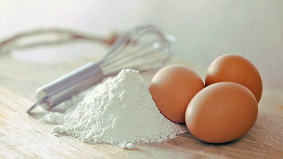 Eier, Mehl und ein Schneebesen auf einer Arbeitsfläche. © fotolia.com Foto: guy
