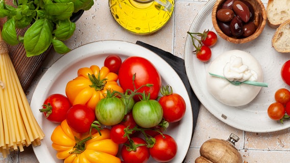 Teller mit bunten Tomaten, Basilikum, Mozzarella, Pfeffermühle und Pasta auf einer Steinplatte © Colourbox Foto: Evgeny Karandaev