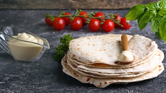 Fladenbrote liegen aufgestapelt auf einem dunklen steinernen Untergrund, darauf ein Holzlöffel mit Mayonnaise © colourbox 