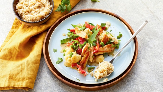 Ein Teller mit einer Hähnchenpfanne mit Gemüse und einem Löffel mit Reis. © Food Still life Foto: Katrin Winner