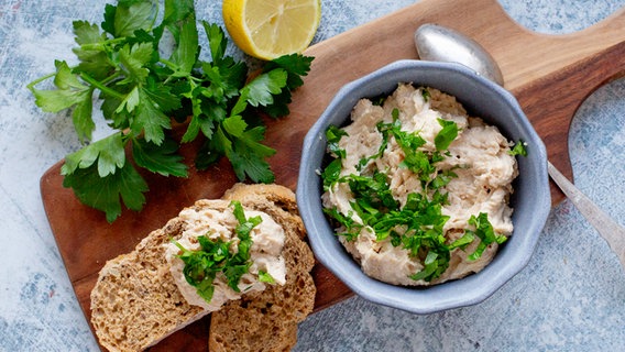 Ein Schälchen mit Bohnenhummus, daneben zwei Scheiben Brot auf einem Brett. © NDR Foto: Claudia Timmann