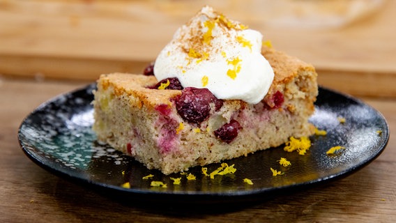 Ein Stück Kirsch-Kartoffel-Kuchen mit Sahne auf einem Teller serviert © NDR Foto: Claudia Timmann