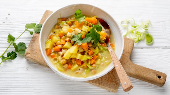 Ein tiefer Teller mit einer Kichererbsen-Gemüsesuppe auf einem Holzbrett. © NDR Foto: Claudia Timmann