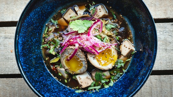 Zucchini-Ramen mit mariniertem Ei und Shiitake in einem dunklen tiefen Teller serviert. © NDR Foto: Tarik Rose