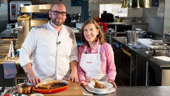 Spitzenkoch Thomas Imbusch und NDR Reporterin Lucia Baumgärtner stehen in einer Restaurantküche vor Tellern mit gebratener Entenkeule und Entenbrust. © NDR Foto: Claudia Timmann