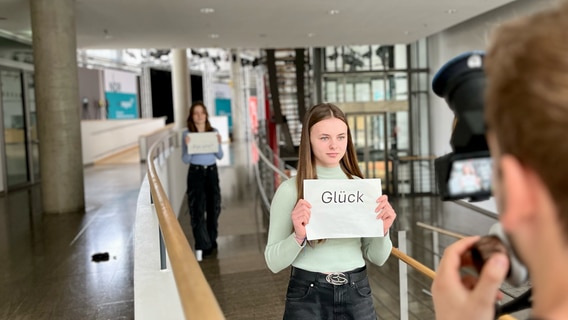 Eine Schülerin hält ein Schild mit dem Wort "Glück" in der Hand. Sie zählt zu den Siegern des NDR einfach.Medien Podclass Contest 2024/25. © NDR 