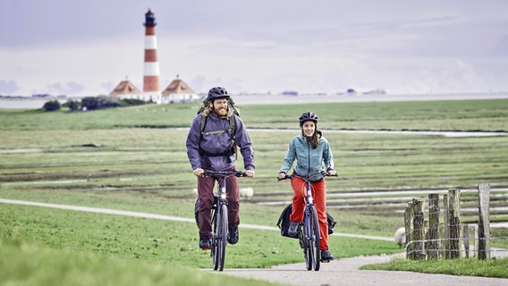 Two cyclists ride through salt marshes near Westerhever, with the lighthouse in the background.  © imago images Photo: Westend61