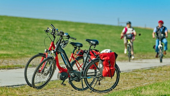 Fahrräder und Radfahrer auf einem Radweg hinter dem Deich in Carolinensiel © IMAGO / blickwinkel 