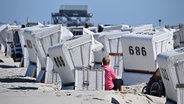 Eine Frau sitzt, an einen Strandkorb gelehnt, in St. Peter Ording am Strand. © dpa Foto: Carsten Rehder