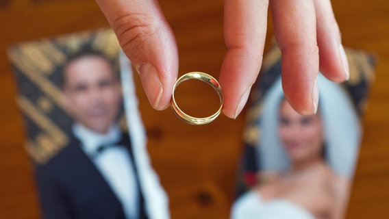 Eine Frau hält mit zwei Fingern einen Ehering über einem zerissenen Hochzeitsfoto. © picture alliance / ZB Foto: Patrick Pleul