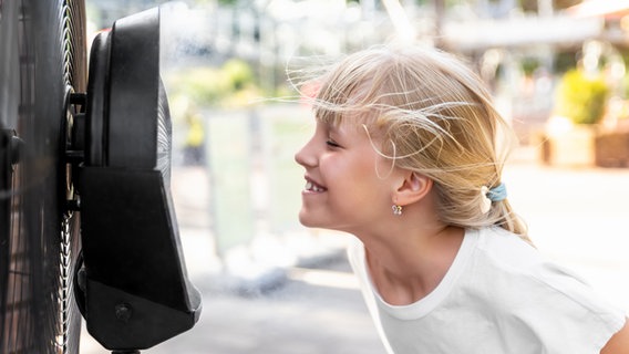 Ein Mädchen steht vor einem Ventilator und kühlt sich. © Colourbox 