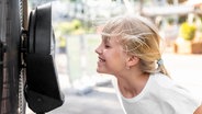 Ein Mädchen steht vor einem Ventilator und kühlt sich. © Colourbox 