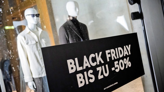 Ein schwarzes Plakat mit der Aufschrift "Black Friday, bis zu minus 50 Prozent" hängt in einem Schaufenster mit Herrenbekleidung. © picture alliance/dpa | Christoph Soeder Foto: Christoph Soeder