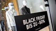 Ein schwarzes Plakat mit der Aufschrift "Black Friday, bis zu minus 50 Prozent" hängt in einem Schaufenster mit Herrenbekleidung. © picture alliance/dpa | Christoph Soeder Foto: Christoph Soeder