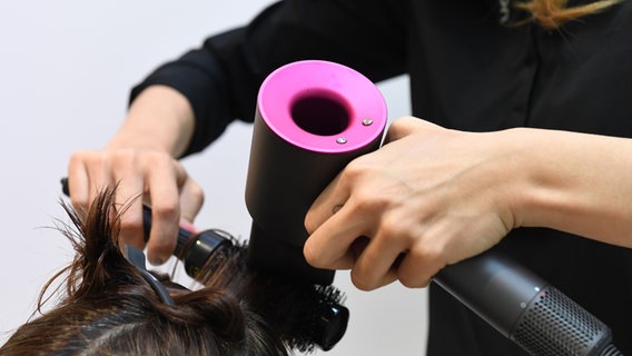 Eine Frau föhnt einer anderen die Haare mit einem Föhn der Marke Dyson. © picture alliance / dpa Themendienst | Andrea Warnecke Foto: Andrea Warnecke