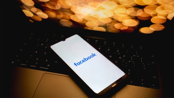 Das Facebook-Logo wird bildschirmfüllend auf einem Handy angezeigt, das auf der Tastatur eines Laptops liegt. © picture alliance / NurPhoto | Nikolas Kokovlis Foto: Nikolas Kokovlis