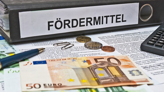 Auf einem Tisch liegen ein Aktenordner mit der Beschriftung "Fördermittel", Geldscheine, ein Taschenrechner und ein Stift. © picture alliance Foto: Zoonar | Stockfotos-MG