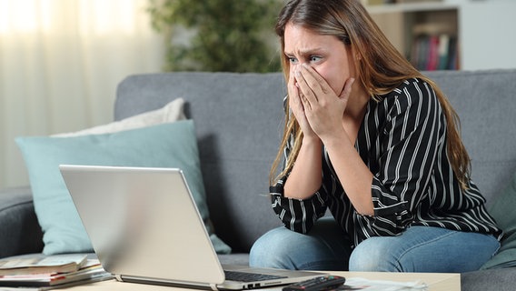 Eine Frau sitzt betroffen vor einem Laptop und hält sich die Hände vor Mund und Nase © colourbox 