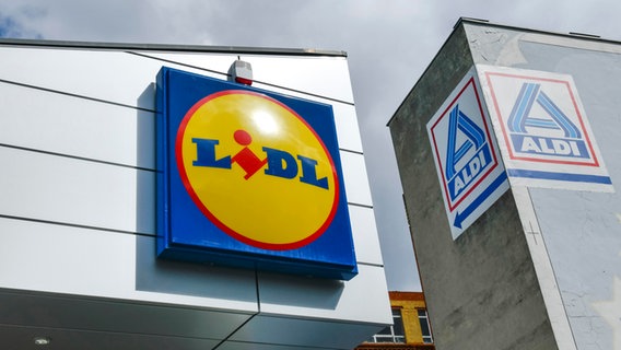 Das Logo einer Lidl-Filiale, dahinter ein Hinweisschild zu einem Aldi-Markt. © picture alliance / picture alliance/Bildagentur-online | Bildagentur-online/Schoening 