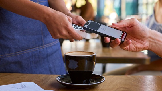 Eine Person zahlt in einem Café mit seinem Smartphone. © picture alliance / Shotshop Foto: Monkey Business 2