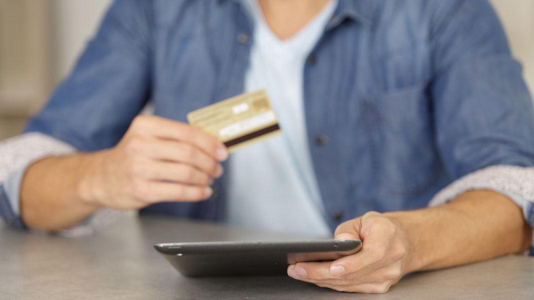 Ein Mann hält ein Tablet und eine Kreditkarte in den Händen.