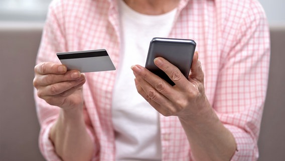 Eine ältere Frau hält eine Kreditkarte in einer und ein Smarphone in der anderen Hand. © colourbox Foto: Motortion