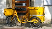 Ein gelbes Postfahrrad der Deutschen Post mit großen Taschen für die Post steht vor einem Gebäude. © picture alliance / CHROMORANGE | Michael Bihlmayer Foto: Michael Bihlmayer