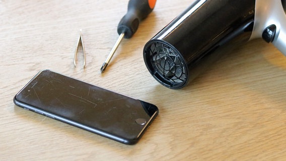 Ein schwarzes Smartphone, ein Schraubenzieher, eine Pinzette und ein Fön, auf einem Tisch liegend. © NDR Foto: Elke Janning