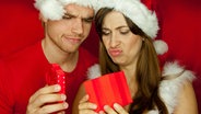 Ein Mann und eine Frau mit Weihnachtsmützen blicken unzufrieden auf ein Geschenk. © Fotolia Foto: drubig-photo