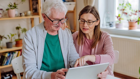 Eine älterer Mann und eine jüngere Frau schauen zusammen auf ein Tablet. © colourbox 