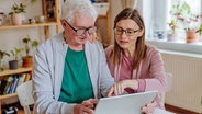 Eine älterer Mann und eine jüngere Frau schauen zusammen auf ein Tablet. © colourbox 