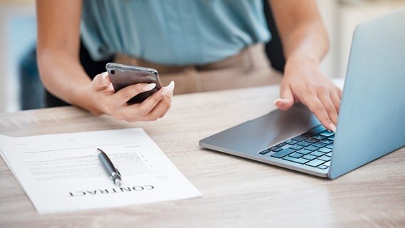 Frau hält ein Handy in der Hand und sitzt am Computer. © Colourbox Foto: Peopleimages.com