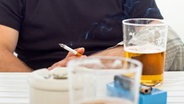 Ein Mann sitzt mit einem Glas Bier an einem Tisch und raucht eine Zigarette. © Colourbox 