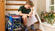 Ein enttäuschter kleine Junge sitzt mit seinem Zeugnis auf der Treppe. © Imago Foto: Bernhard Classen